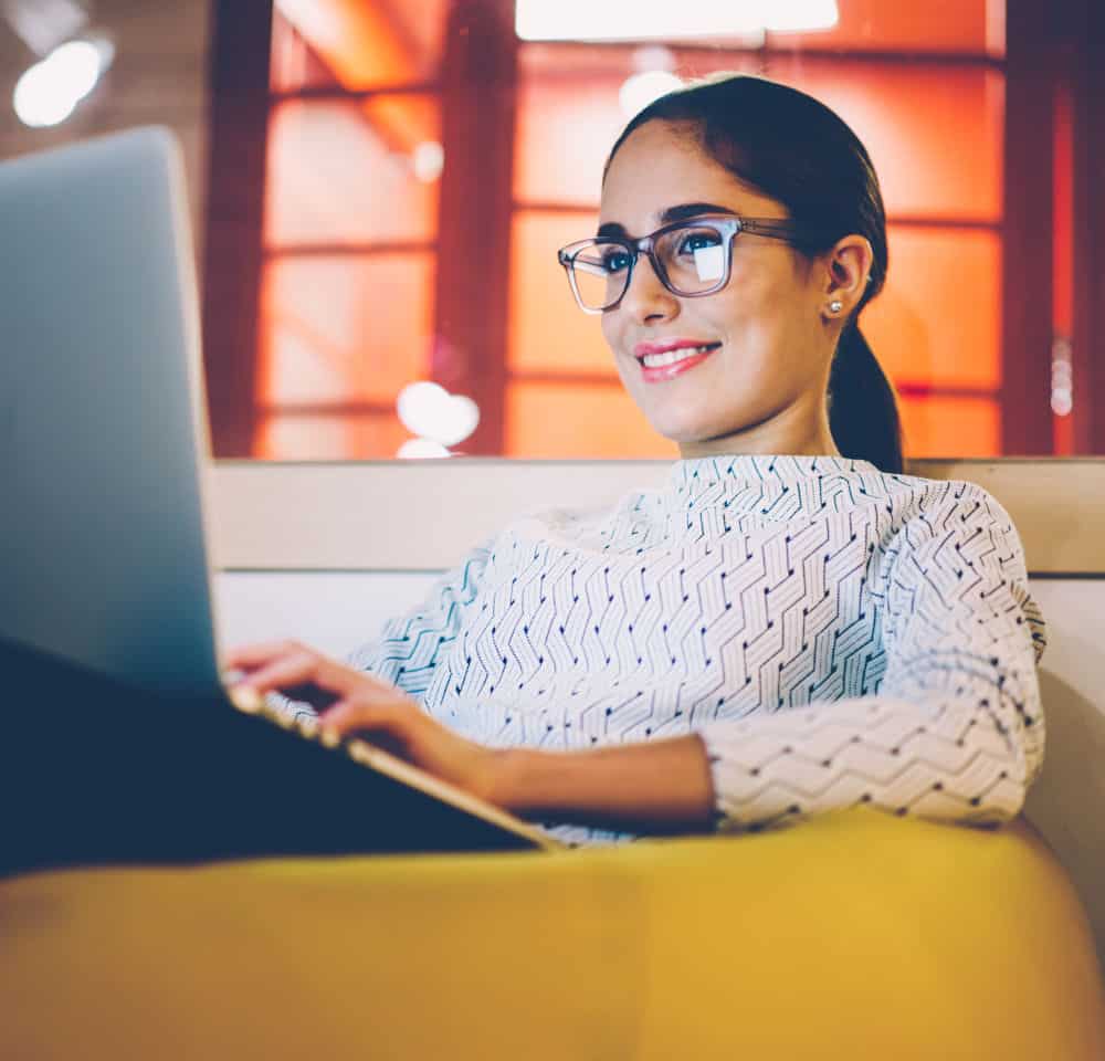 Smiling woman watching video on laptop computer working on freelance in cozy coworking interior,female student resting during free time reading news blogging in social networks using netbook